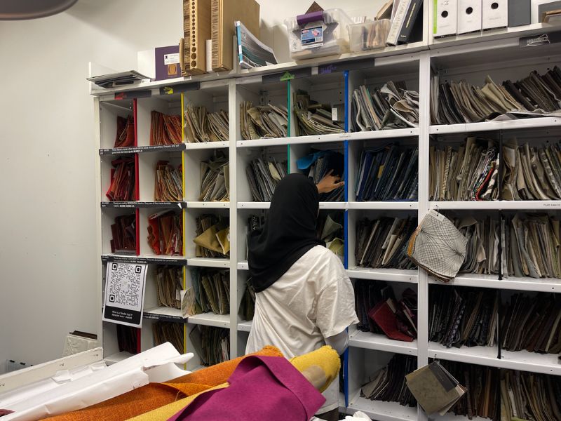 A girl wearing a hijab with her back towards the camera and looking through a shelf filled with books and folders